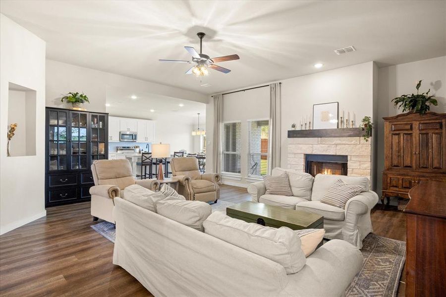 Living room with recessed lighting, dark wood-type flooring, ceiling fan, and a stone fireplace