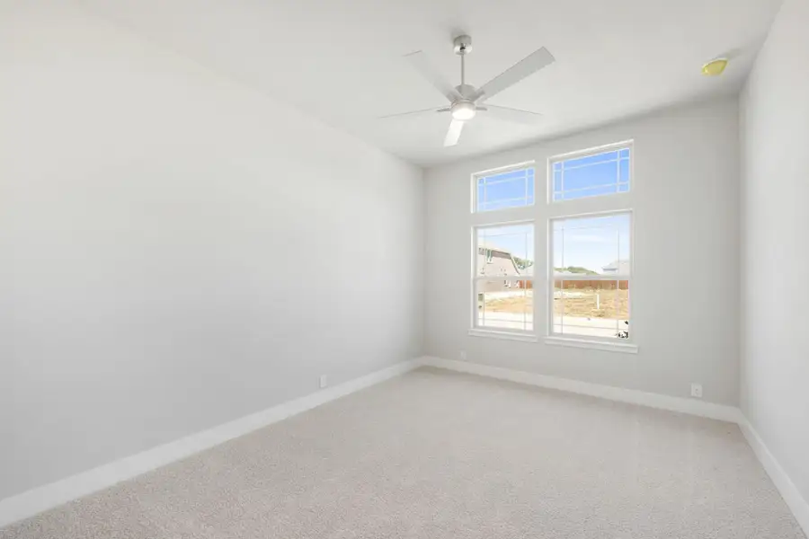 Empty bedroom with carpet flooring, ceiling fan, and double windows with transom panels