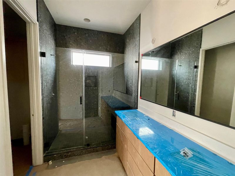 The bathroom features a glass-enclosed shower with dark tiled walls, a window, and a vanity with a large mirror