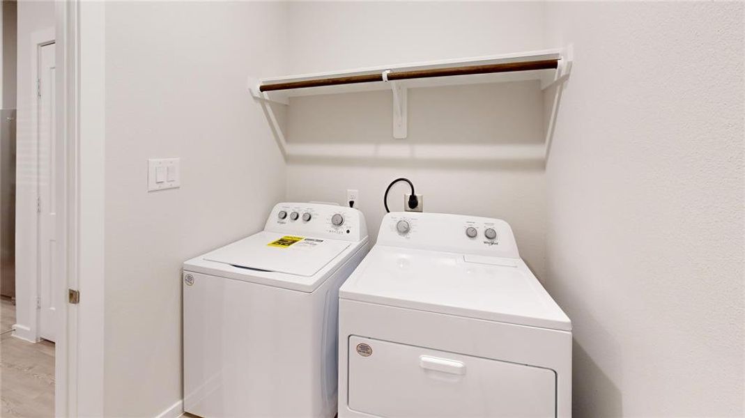 This photo showcases a laundry area with a washer and dryer set beneath a wooden shelf, set against a neutral wall.