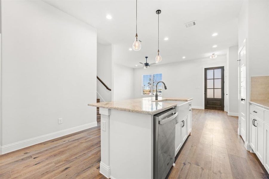 Kitchen featuring decorative light fixtures, an island with sink, light hardwood / wood-style floors, white cabinets, and dishwasher