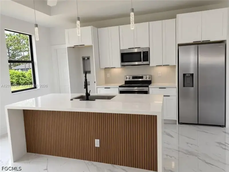 Kitchen featuring white shaker-style cabinetry, quartz countertops, a central island with a slatted wood-finish base, stainless steel appliances, and large-format tile flooring