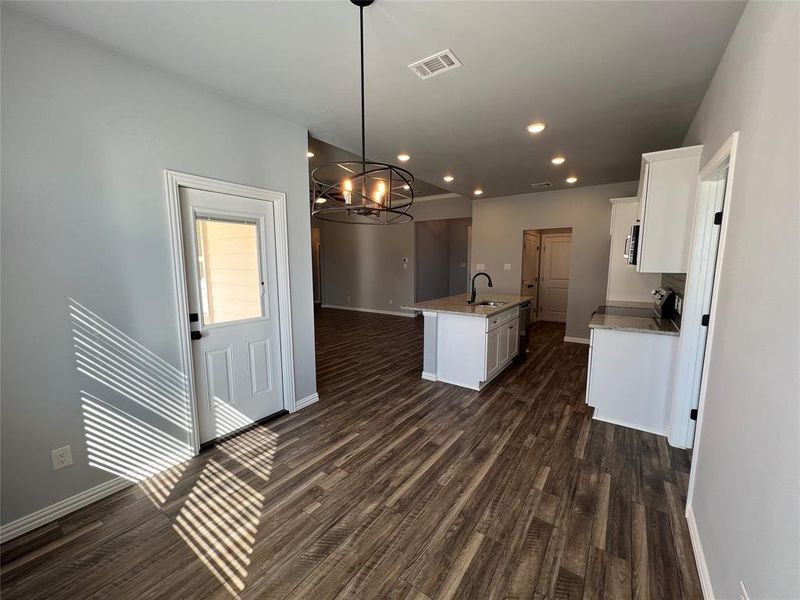 Kitchen with a kitchen island with sink, sink, decorative light fixtures, dark hardwood / wood-style floors, and white cabinetry