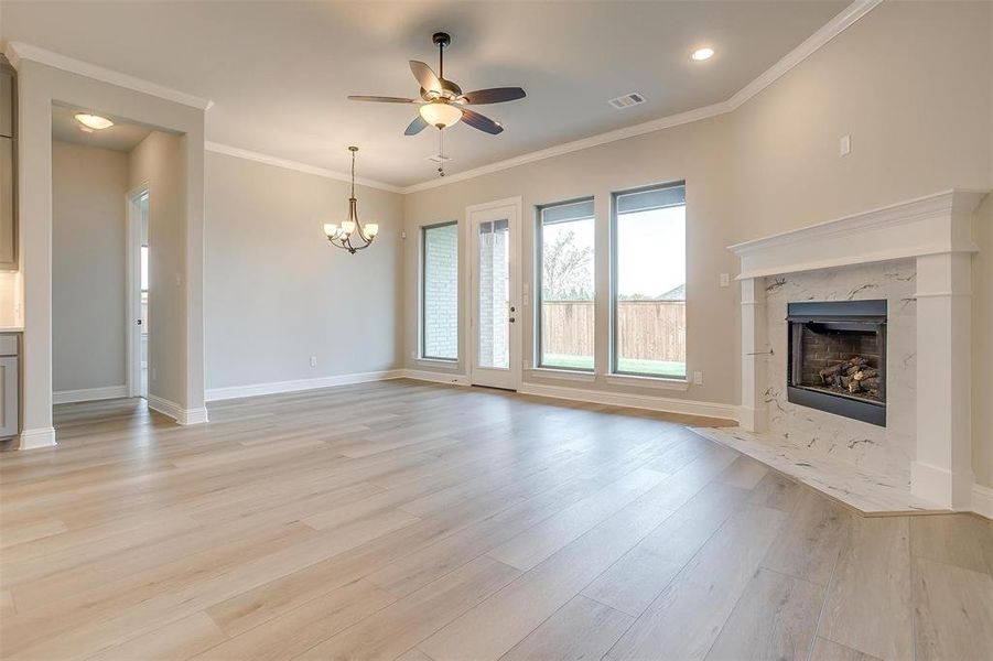 Unfurnished living room featuring ceiling fan with notable chandelier, a premium fireplace, light hardwood / wood-style flooring, and ornamental molding