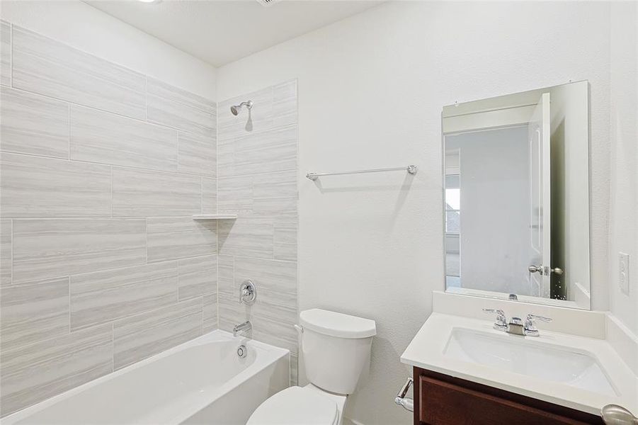 Full bathroom featuring vanity, tiled shower / bath combo, and toilet