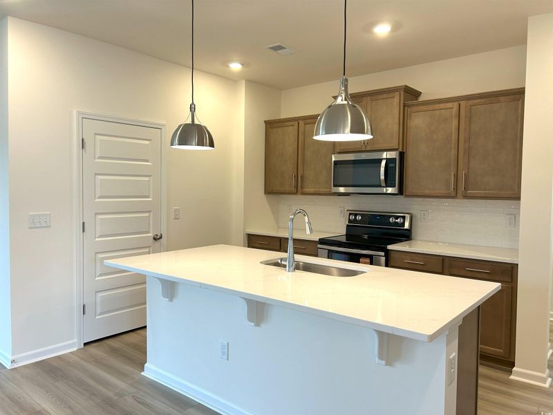 Kitchen featuring appliances with stainless steel finishes, light wood finished floors, decorative backsplash, a kitchen breakfast bar, and light countertops