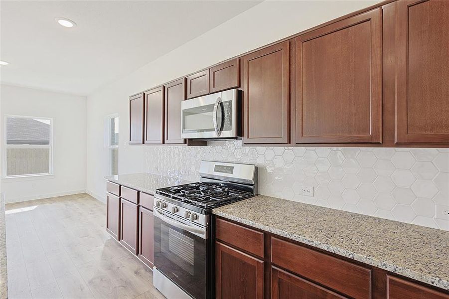 Kitchen featuring tasteful backsplash, light stone countertops, light hardwood / wood-style flooring, and stainless steel appliances