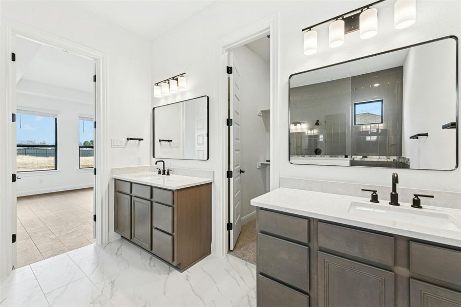 Full bathroom featuring a tile shower, two vanities, and light marble finish flooring