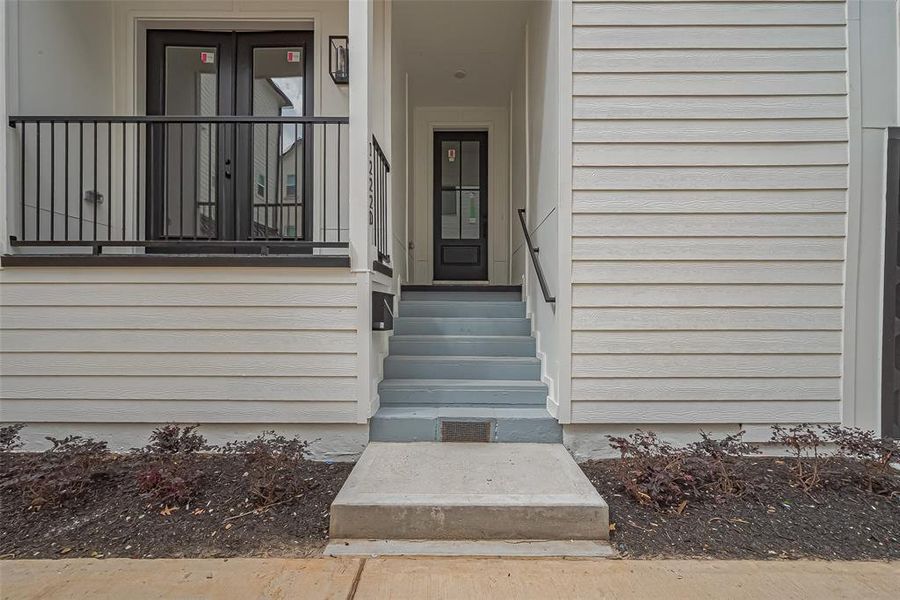 Step into modern elegance with this entryway, featuring a sleek staircase, abundant natural light from a large window, and a chic black door. The neutral walls and floors enhance the welcoming, spacious ambiance.