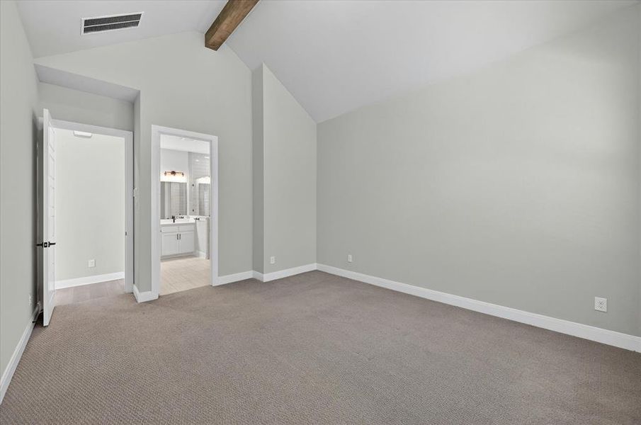 Spacious room featuring vaulted ceilings with a wood beam, light grey wall paint, and grey carpet flooring Spacious room featuring vaulted ceilings with a wood beam, light grey wall paint, and grey carpet flooring