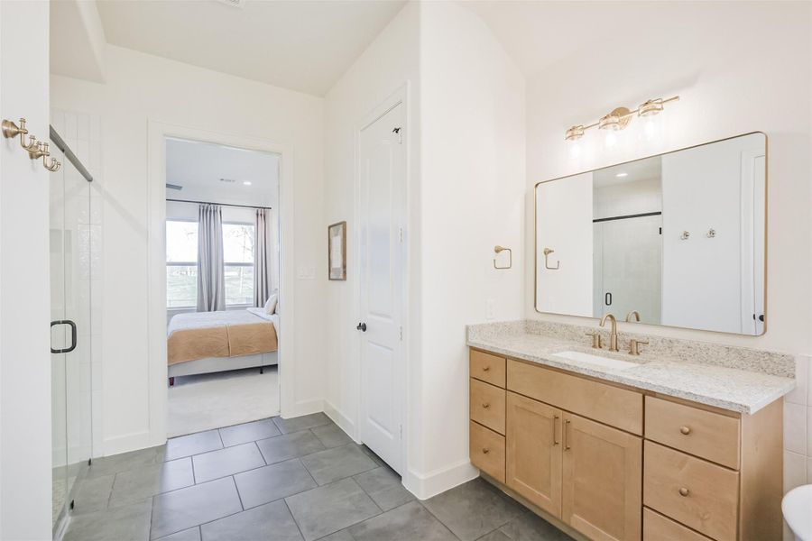The vanities granite countertops and natural colored cabinetry provide the perfect contrast for the grey tiled floor.