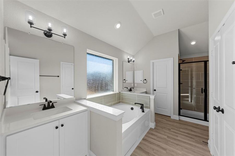 Bathroom with two vanities, lofted ceiling, a stall shower, a garden tub, and light wood finished floors