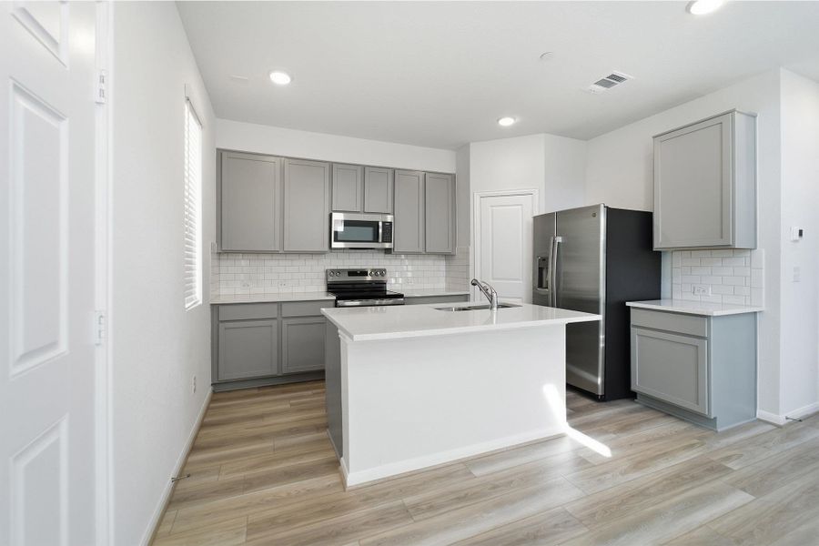 Kitchen with gray cabinetry, stainless steel appliances, an island with sink, light wood-type flooring, and recessed lighting