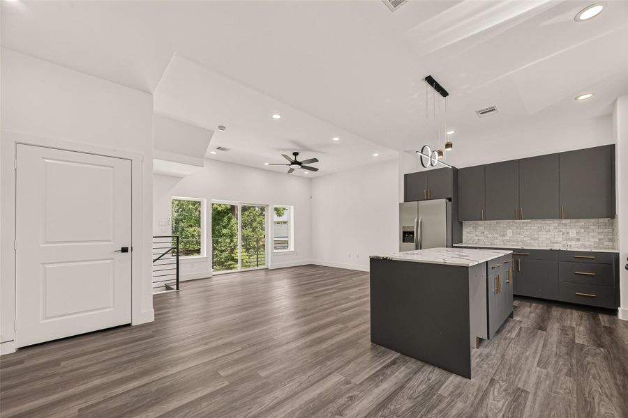 This modern open-concept space features sleek gray cabinetry and stainless steel appliances in the kitchen, with a spacious island. The living area boasts large windows for ample natural light and a ceiling fan, all highlighted by elegant wood flooring. This modern open-concept space features sleek gray cabinetry and stainless steel appliances in the kitchen, with a spacious island. The living area boasts large windows for ample natural light and a ceiling fan, all highlighted by elegant wood flooring.