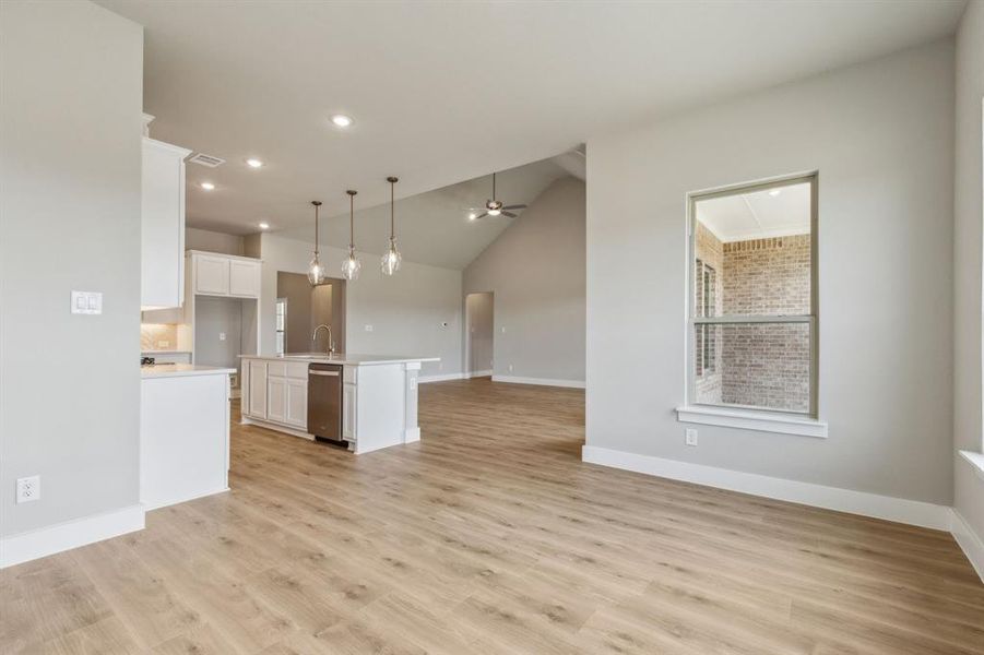 Kitchen featuring decorative light fixtures, stainless steel dishwasher, white cabinetry, light hardwood / wood-style flooring, and a kitchen island with sink