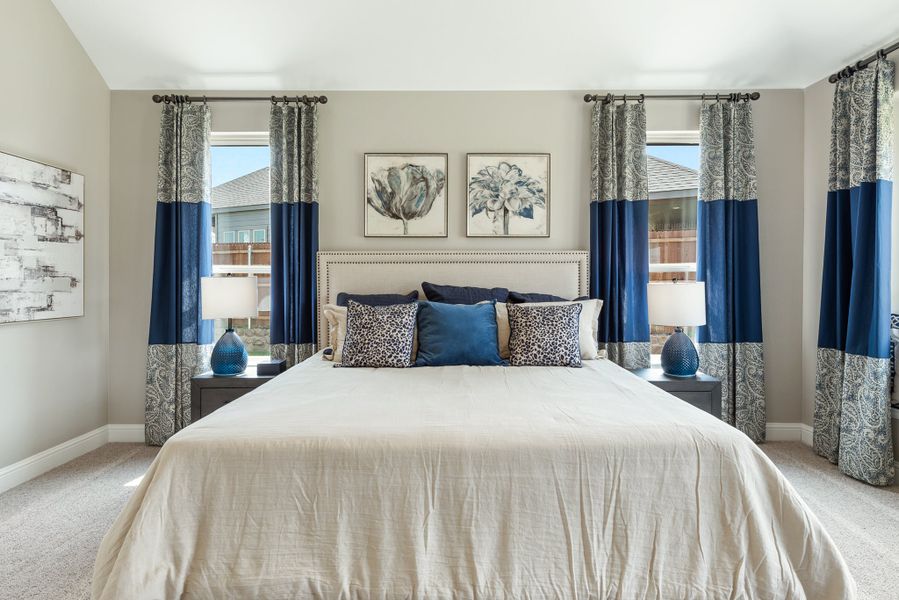 Bedroom with king bed, upholstered headboard, blue accent pillows, and navy curtains flanking two windows