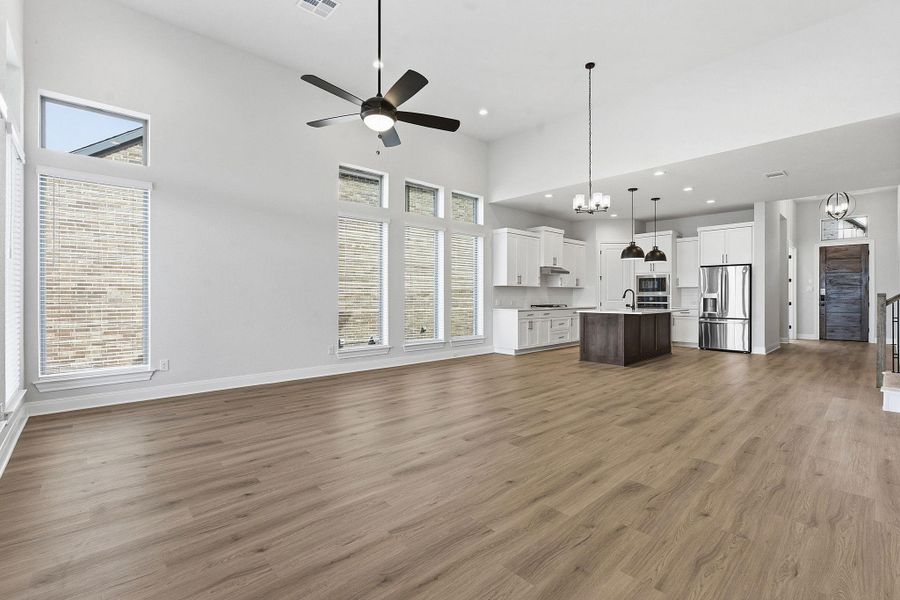 Unfurnished living room featuring a high ceiling, suspended lighting, a ceiling fan, and light wood-type flooring
