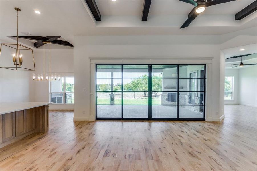 Living room featuring ceiling fan with notable chandelier, beam ceiling, and light hardwood / wood-style floors. Great views to the outdoor living area