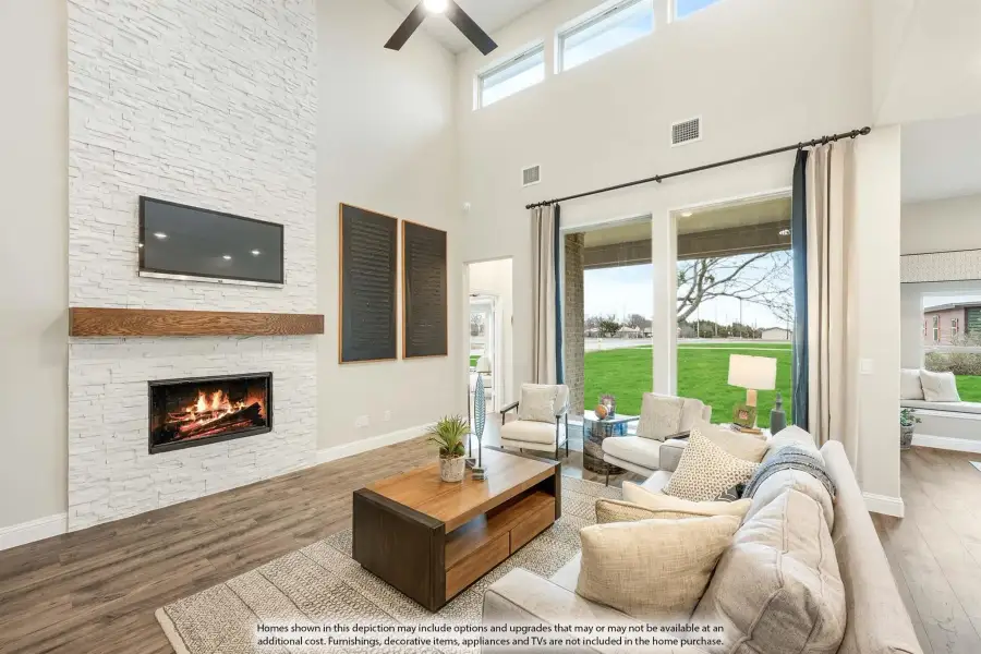 Living room with two-story stone fireplace, hardwood floors, and large windows overlooking a backyard
