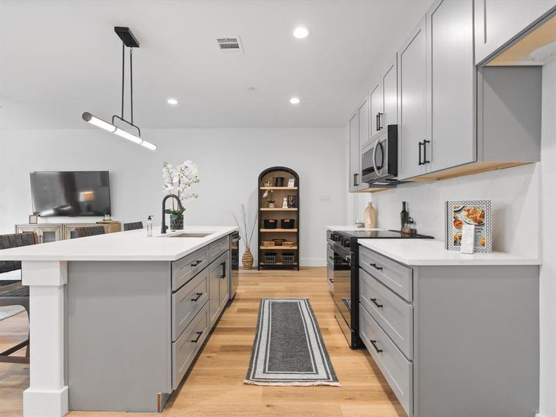 Kitchen featuring gray cabinetry, stainless steel microwave, black range with electric cooktop, and a sink Kitchen featuring gray cabinetry, stainless steel microwave, black range with electric cooktop, and a sink