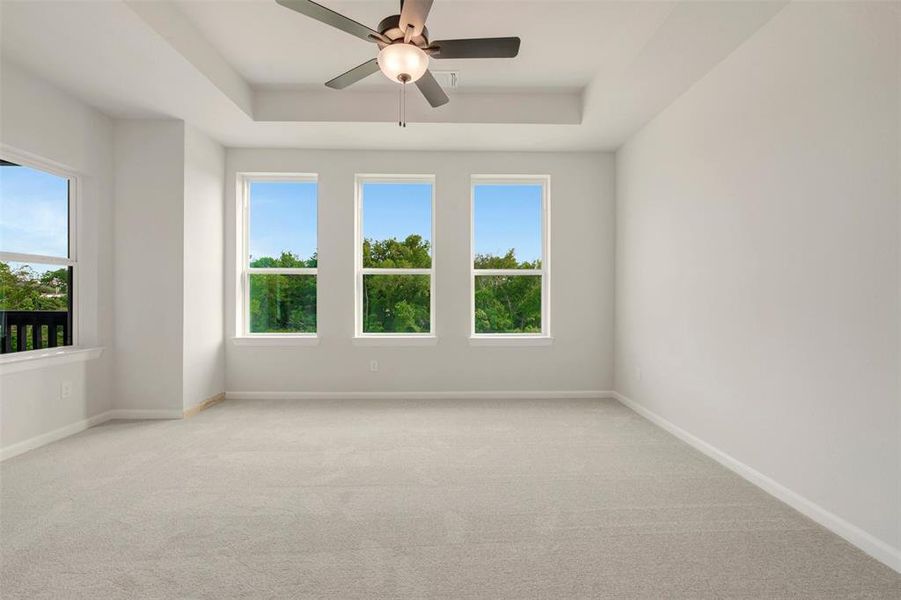 Spacious room featuring light-toned carpet flooring, a tray ceiling, and a ceiling fan with integrated lighting Spacious room featuring light-toned carpet flooring, a tray ceiling, and a ceiling fan with integrated lighting
