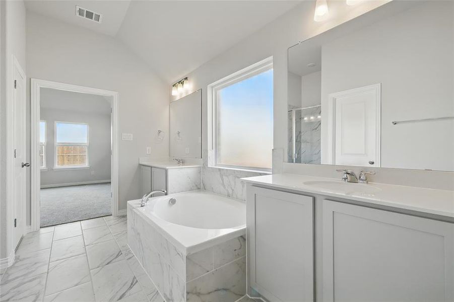 Full bath featuring light marble finish floors, two vanities, a garden tub, a marble finish shower, and vaulted ceiling Full bath featuring light marble finish floors, two vanities, a garden tub, a marble finish shower, and vaulted ceiling