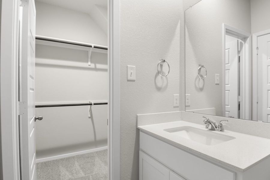 Image of primary bathroom with white cabinets and mirror with vanity and a walk in closet