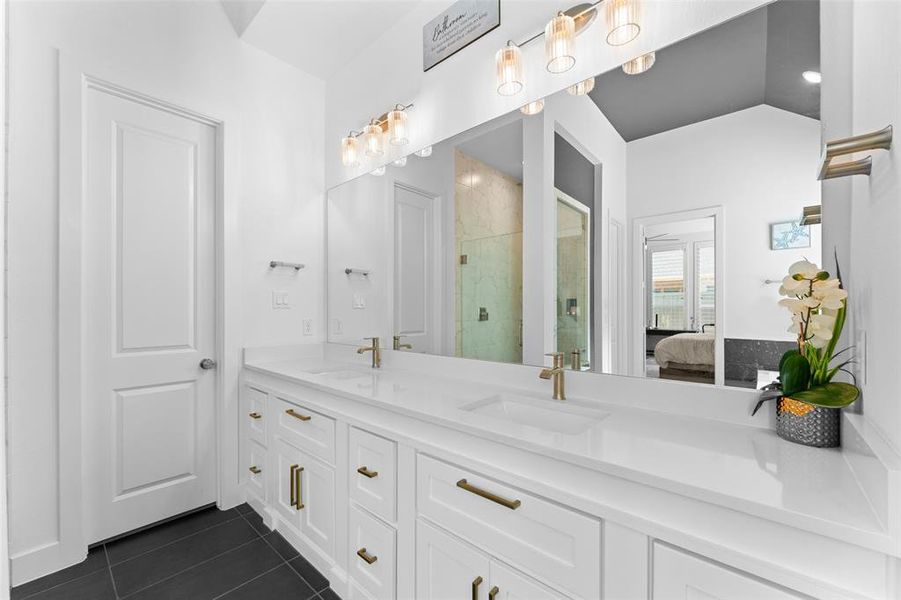 The bathroom features a double vanity with white cabinetry, light-colored countertops, and gold-toned hardware