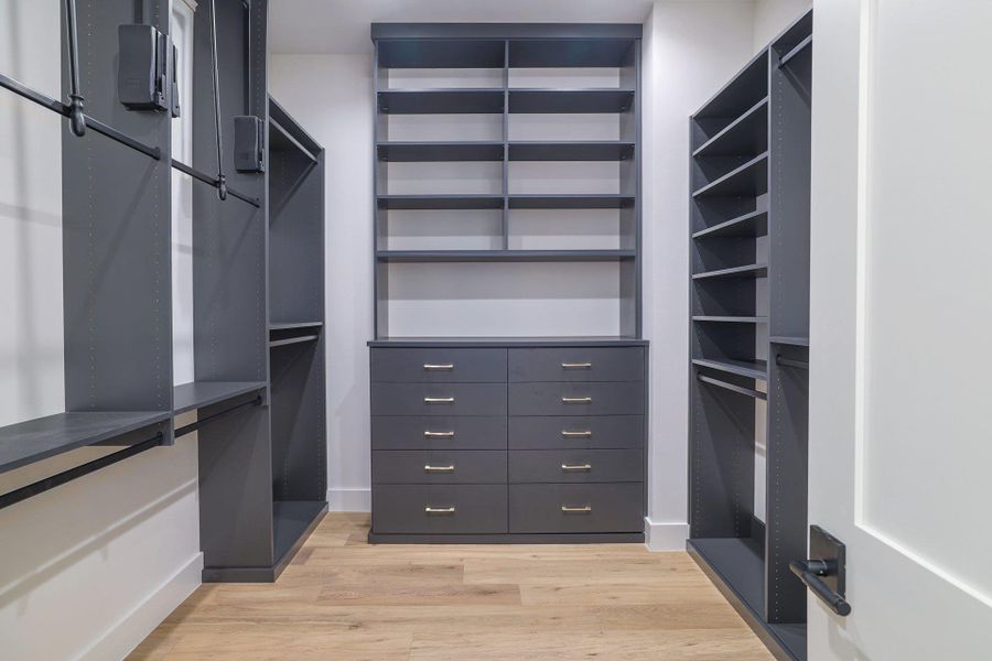 Custom walk-in closet featuring built-in cabinetry, shelving, multiple hanging rods, and a central dresser unit with brushed nickel hardware