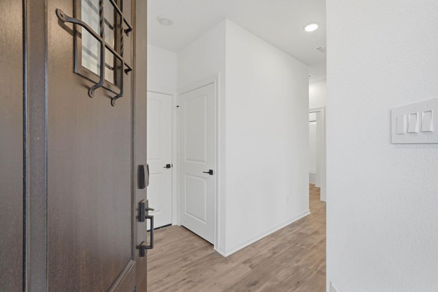 Step through a modern door with iron accents into a bright hallway, where warm warm floors set a fresh and inviting tone.