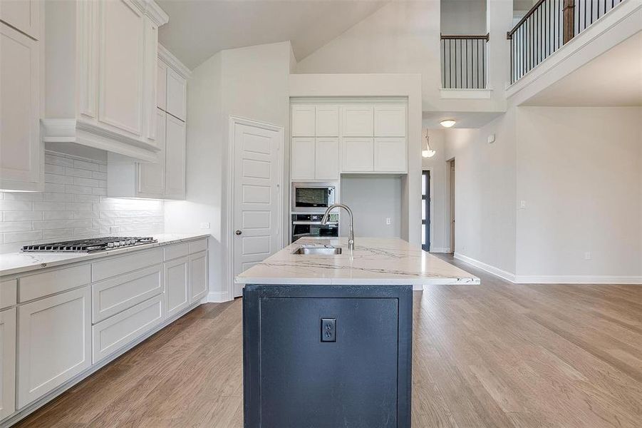 Kitchen featuring light stone counters, light hardwood / wood-style floors, a kitchen island with sink, white cabinetry, and stainless steel appliances