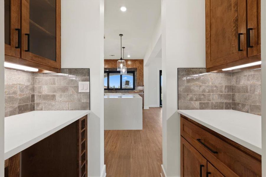 Kitchen featuring backsplash, glass insert cabinets, decorative light fixtures, light stone countertops, and recessed lighting