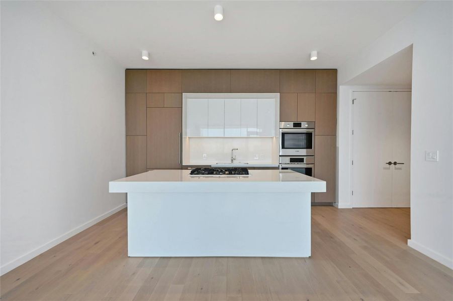 A streamlined culinary space highlighted by Bosch appliances, a gas cooktop built into the expansive quartz island, and custom cabinetry that seamlessly conceals the refrigerator and dishwasher for a clean, modern aesthetic.