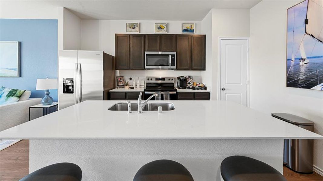 Kitchen with dark wood-style flooring, dark wood finish cabinets, stainless steel appliances, a kitchen bar, and a kitchen island with sink