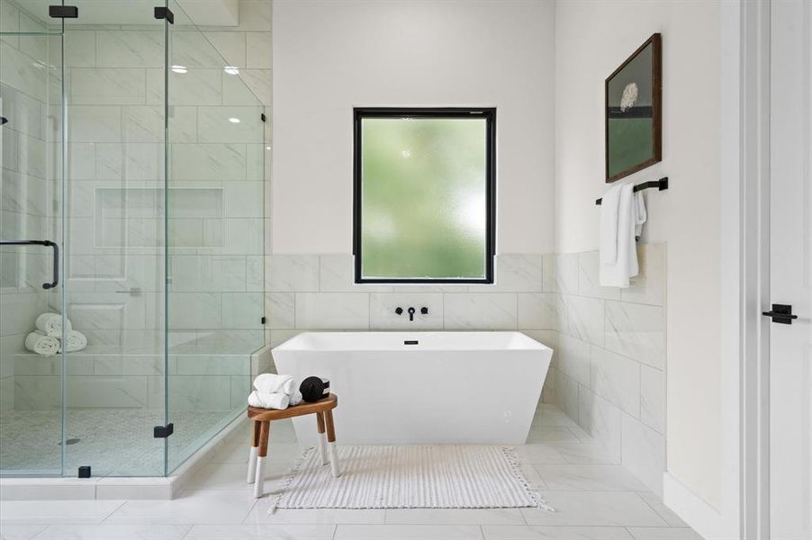 Primary bathroom with a glass shower, freestanding tub, frosted window, and minimalistic decor.