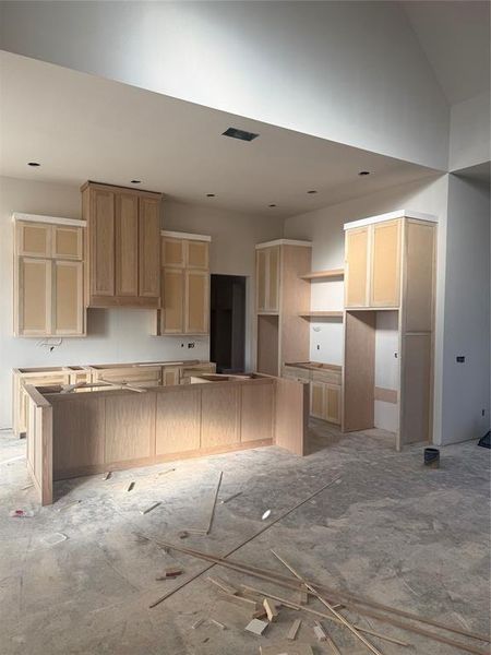 Kitchen with light brown cabinetry, a center island, and vaulted ceiling