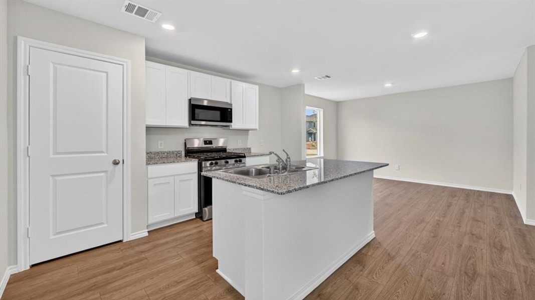 Kitchen featuring a central island with an undermount double sink, stainless steel appliances, white cabinetry, and light-toned countertops