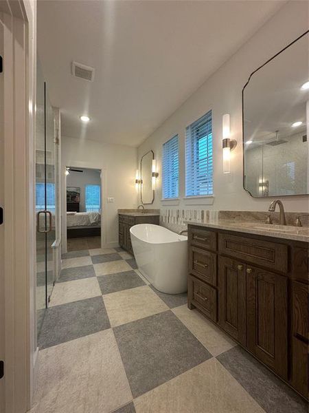 Spacious bathroom featuring a freestanding soaking tub, dual vanity with undermount sinks, separate glass-enclosed shower, and checkerboard floor tiling