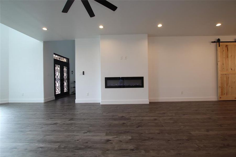 Unfurnished living room featuring a glass covered fireplace, a barn door, dark wood-style floors, recessed lighting, and ceiling fan Unfurnished living room featuring a glass covered fireplace, a barn door, dark wood-style floors, recessed lighting, and ceiling fan