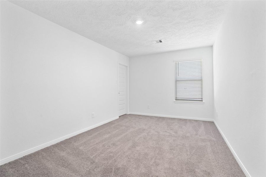This secondary bedroom offers comfort and style with plush carpeting, neutral paint tones, recessed lighting, a large window with blinds, and a walk-in closet.