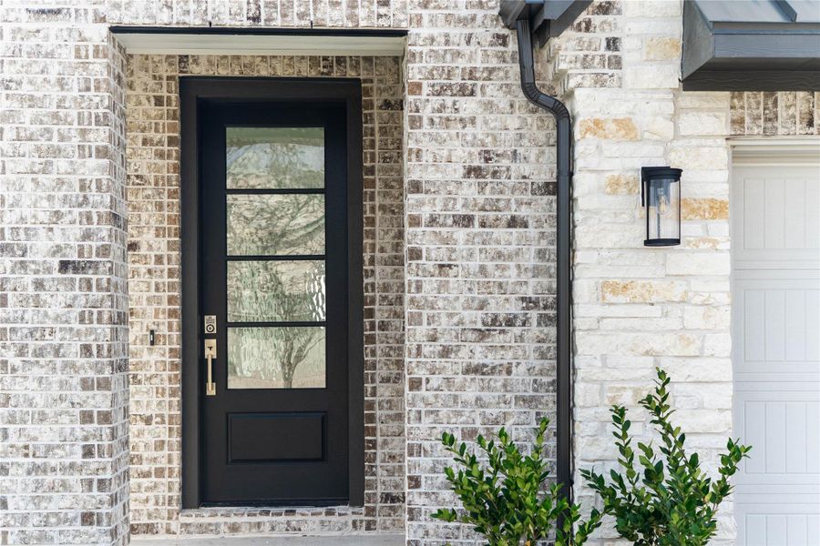 As you walk up to this beautiful home, you notice the stone and brick elevation with contemporary black wall sconce light fixture. The inviting front door is accentuated by a brass-toned handle set contributing to the strong curb appeal.