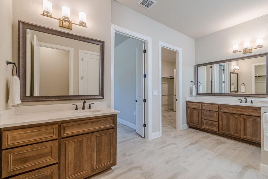 Full bath featuring visible vents, two vanities, a sink, and wood finished floors