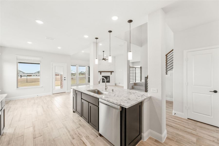 Kitchen island with dark cabinets, granite countertop, and sink open to living area with fireplace Kitchen island with dark cabinets, granite countertop, and sink open to living area with fireplace