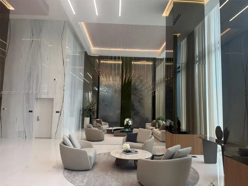 Grand lobby featuring floor-to-ceiling stone wall cladding, polished flooring, integrated linear recessed lighting, a multi-story water feature, and dark reflective wall paneling