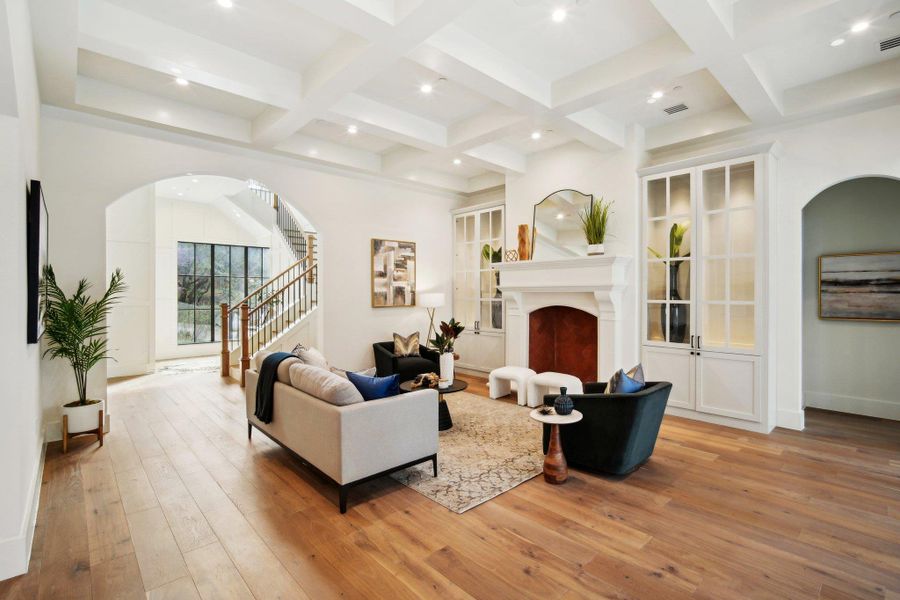 Living area featuring stairway, beam ceiling, a fireplace, light wood-style floors, and coffered ceiling