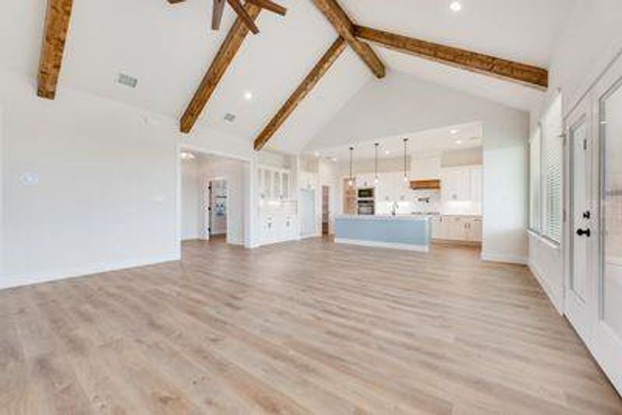 Unfurnished living room with light hardwood / wood-style floors, high vaulted ceiling, beamed ceiling, and ceiling fan