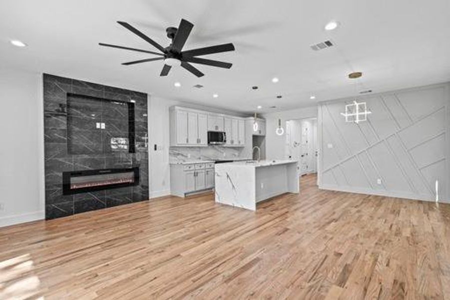 Kitchen featuring hanging light fixtures, light hardwood / wood-style flooring, an island with sink, a tiled fireplace, and white cabinets