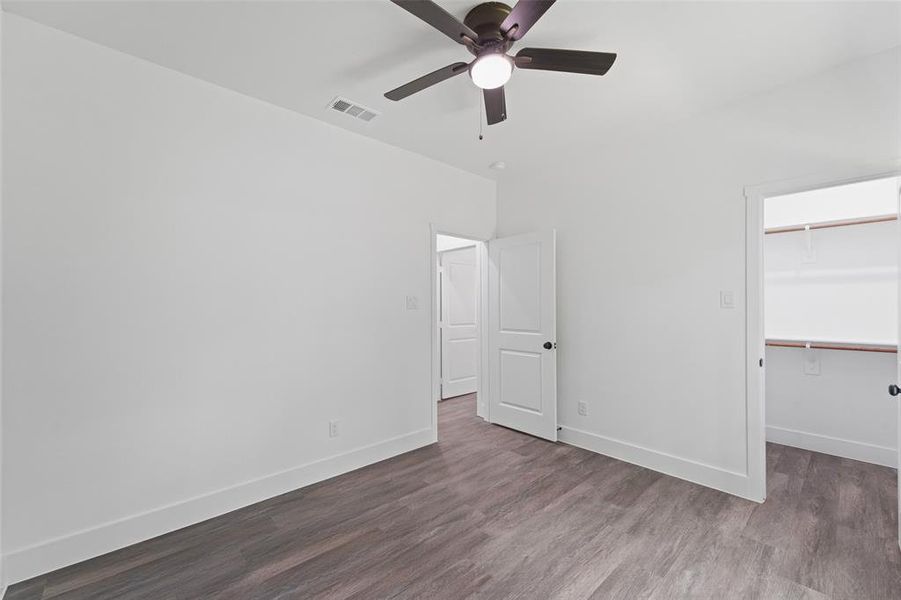 Interior room with wood-finish flooring, white walls, and a ceiling fan Interior room with wood-finish flooring, white walls, and a ceiling fan