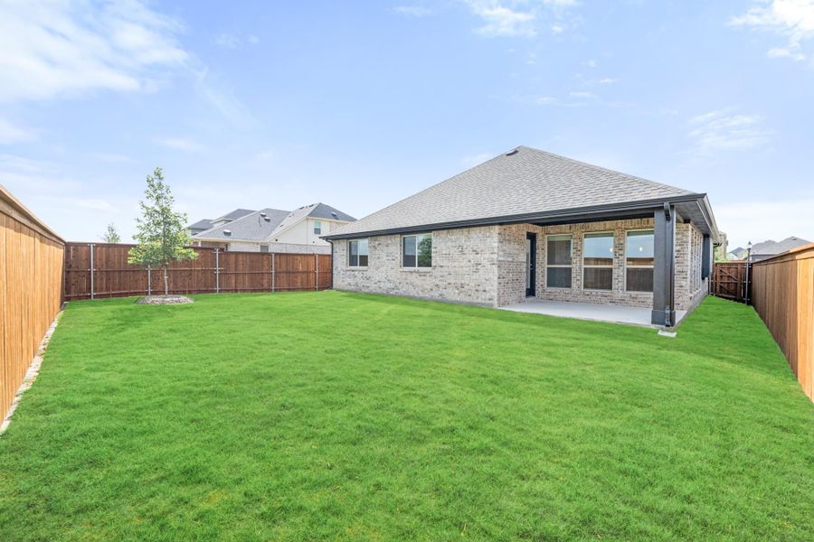 Brick home rear exterior with covered patio, large grassy backyard, and wood privacy fence Brick home rear exterior with covered patio, large grassy backyard, and wood privacy fence