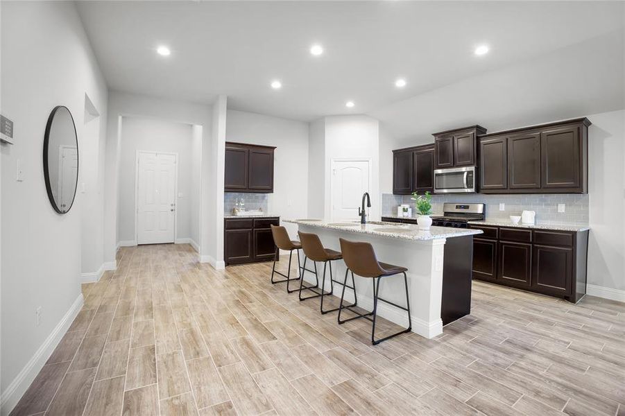 Kitchen featuring tasteful backsplash, recessed lighting, dark brown cabinets, a kitchen bar, and stainless steel appliances
